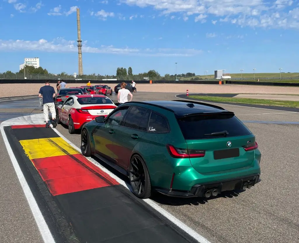 Grüner BMW M3 Touring mit schwarzen Felgen und Sportdiffusor in der Boxengasse beim Drifttraining auf dem Sachsenring, im Hintergrund weitere Fahrzeuge und der charakteristische Kühlturm.