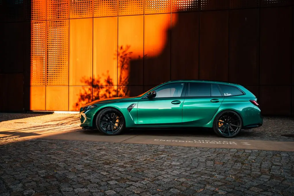 Isle of man grüner BMW M3 Touring vor moderner, orange angestrahlter Metallfassade im warmen Morgenlicht, fotografiert im urbanen Umfeld.
